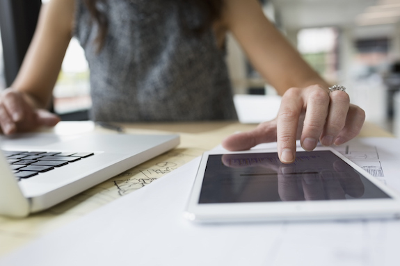 Person working on both a laptop and a tablet on a desk.